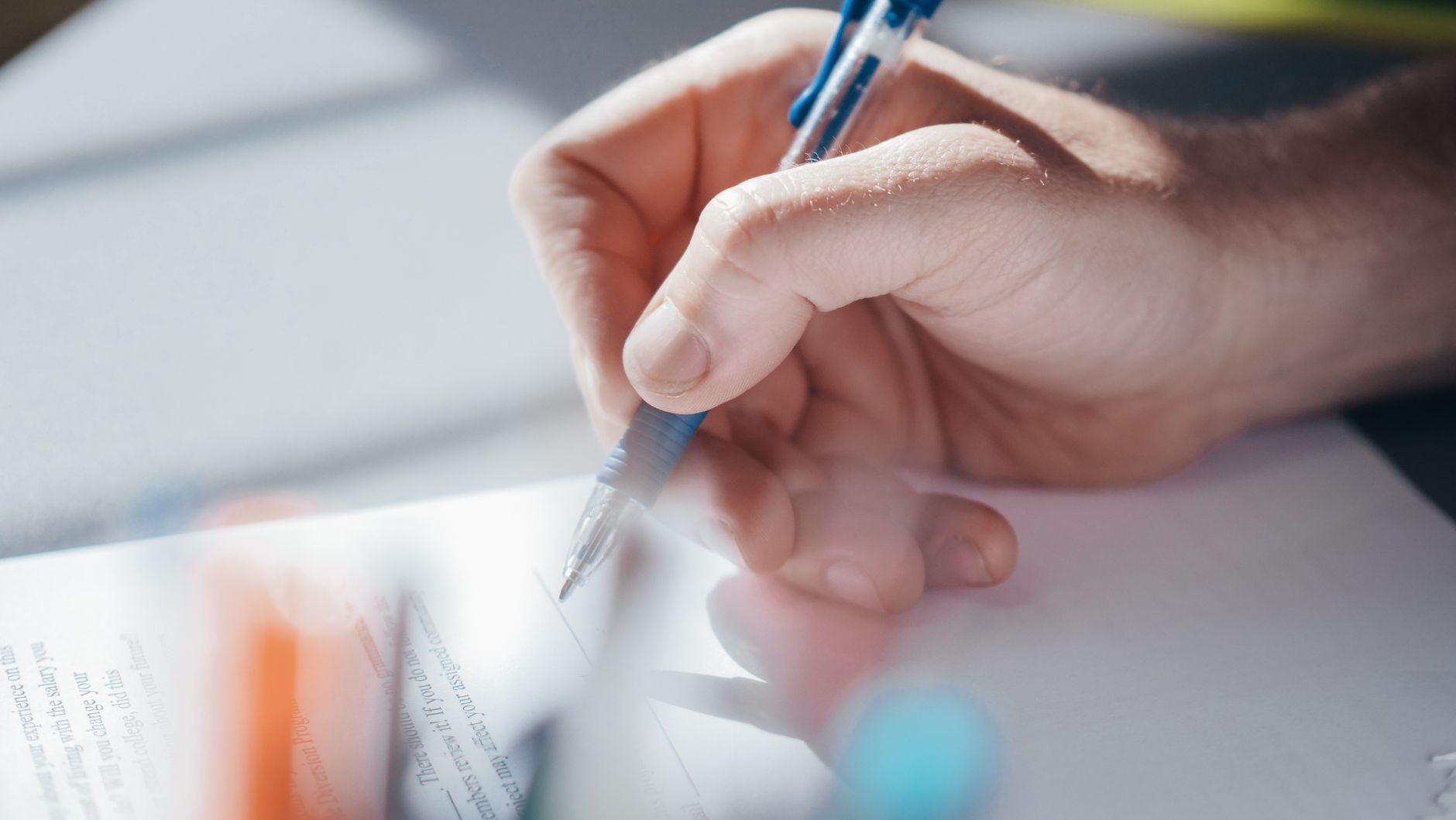 A person writes on a page with a blue pen; English text is visible.